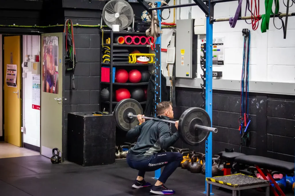 Athlete performing a barbell back squat at full depth with heels flat and torso braced