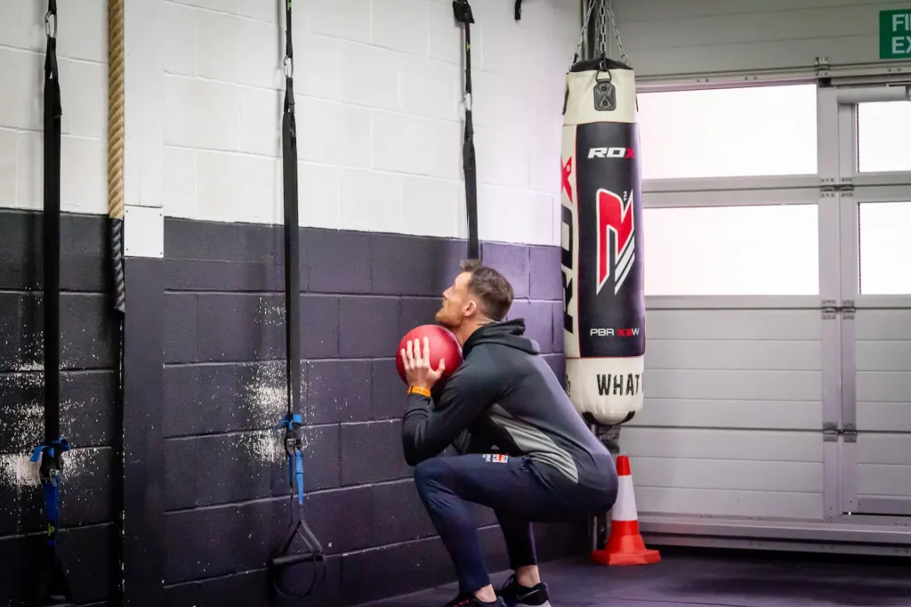 Athlete holding a medicine ball at chest height in the bottom of a squat before throwing to a wall