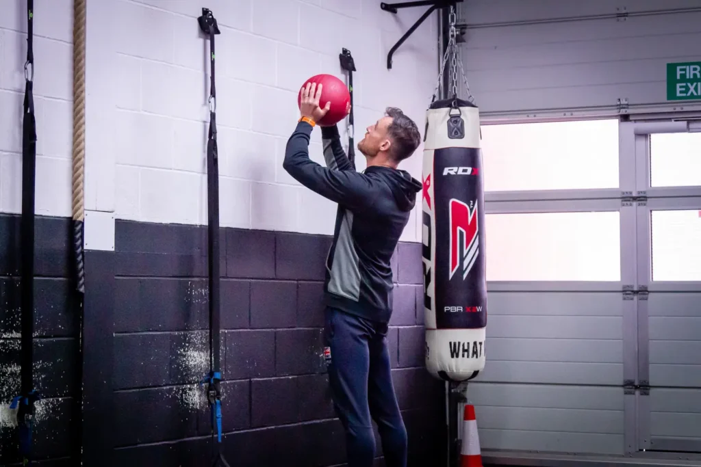 Athlete extending hips and arms to throw a medicine ball upward against a wall